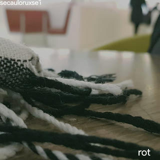 a close up photograph of a black and white scarf on a table, blurred chairs can be seen behind it