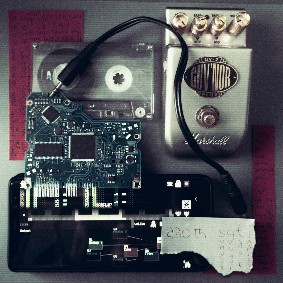 a photograph of a composition of guv'nor guitar pedal, casette tape, a smartphone with sunvox open, some circuit board from hdd, a short jack-jack cable and a few pieces of red and white paper with some things written on it.